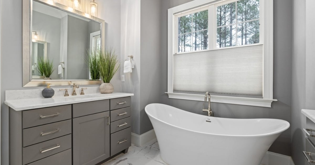 Stock image of modern bathroom with freestanding tub, gray vanity, marble tile floor, and large window in Northern CA