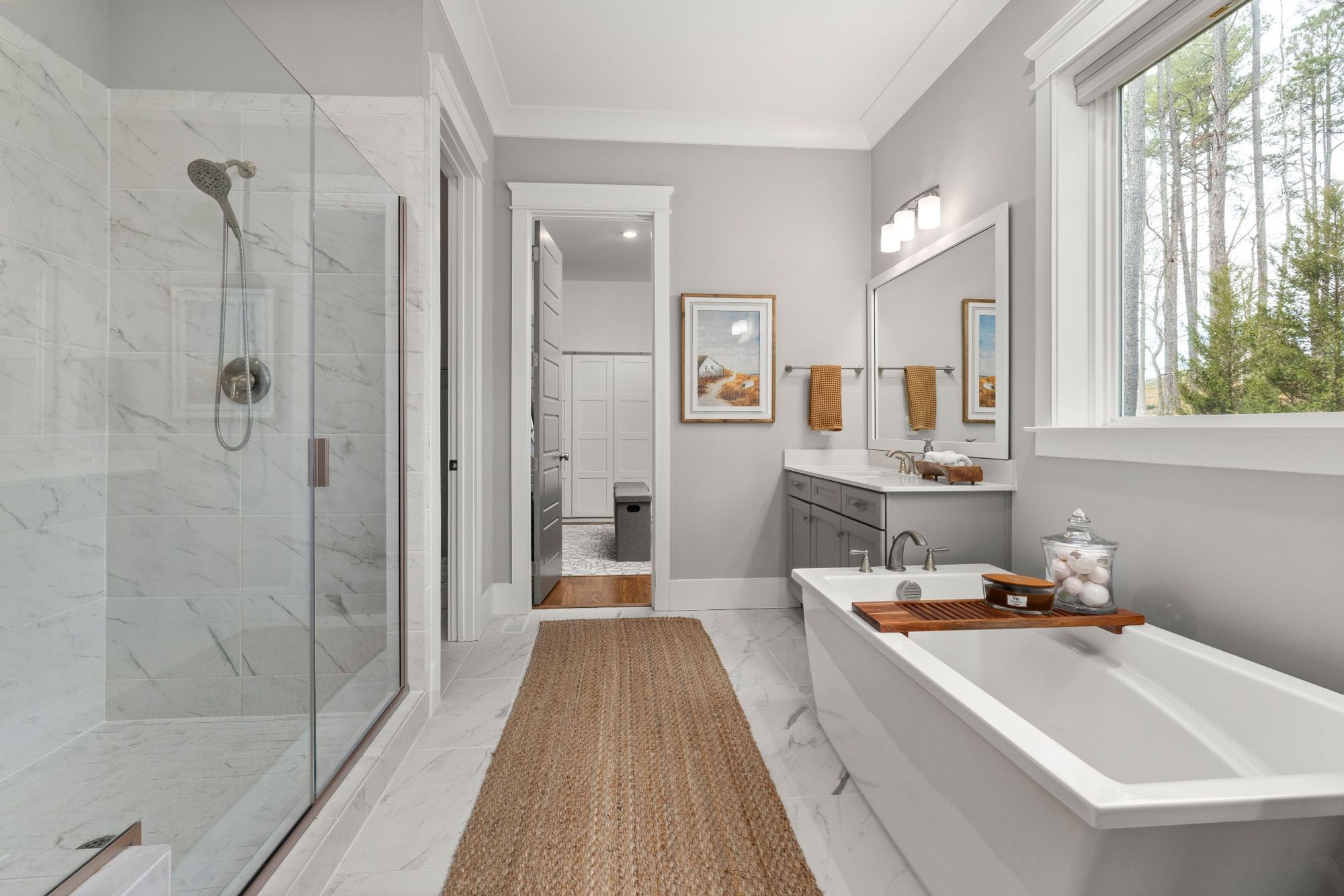 Stock image of modern bathroom with glass shower, soaking tub, gray vanity, and marble tile finishes - optimized