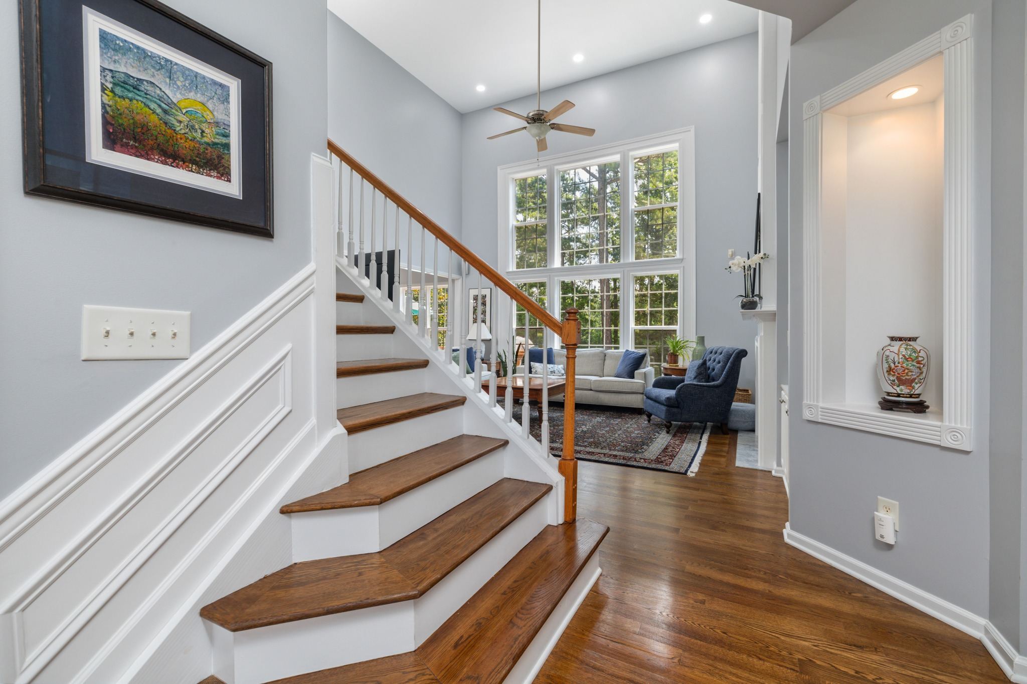 Stock image of a bright foyer with hardwood staircase, tall windows, and sitting area in Northern California -optimized